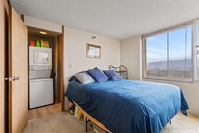 carpeted bedroom featuring multiple windows, a textured ceiling, and stacked washing maching and dryer