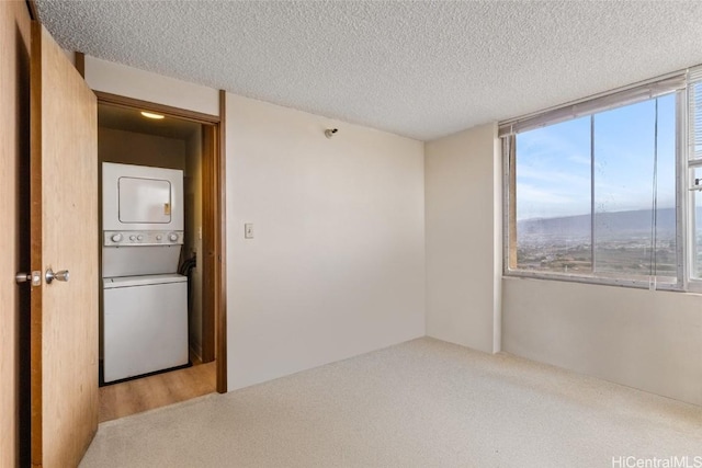 carpeted empty room featuring stacked washer and clothes dryer and a textured ceiling