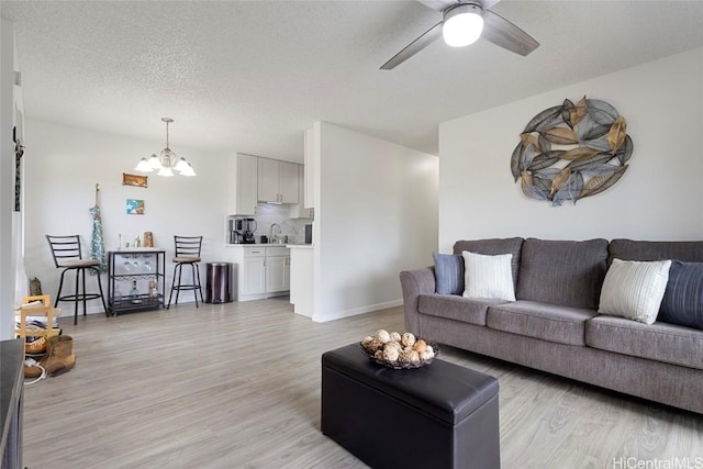 living room with light wood-type flooring, ceiling fan with notable chandelier, a textured ceiling, and sink