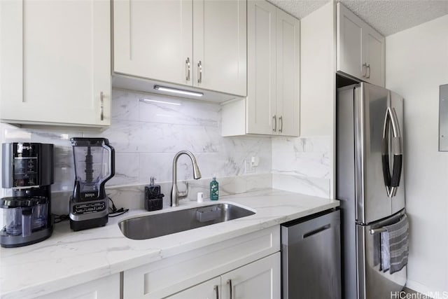 kitchen featuring light stone countertops, appliances with stainless steel finishes, a textured ceiling, sink, and white cabinets