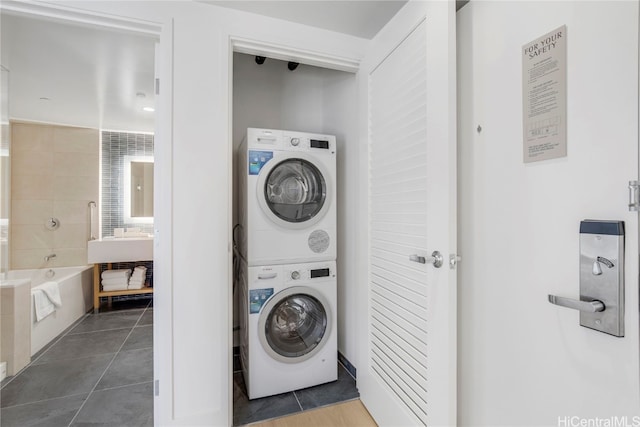 clothes washing area with dark tile patterned flooring and stacked washer and dryer