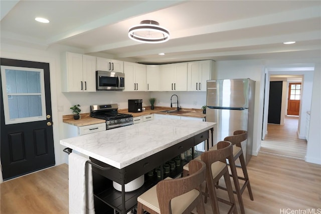 kitchen featuring sink, stainless steel appliances, light hardwood / wood-style floors, white cabinets, and beamed ceiling