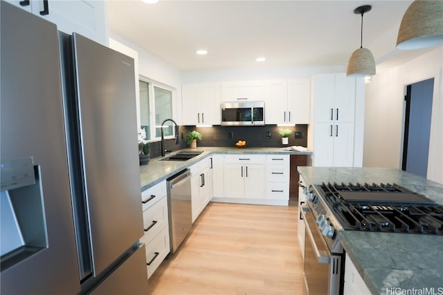 kitchen featuring pendant lighting, white cabinetry, sink, stainless steel appliances, and light wood-type flooring