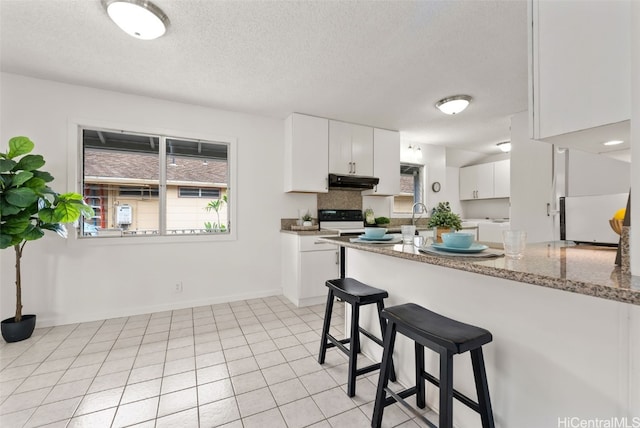 kitchen featuring a kitchen bar, light stone counters, a textured ceiling, electric stove, and white cabinets