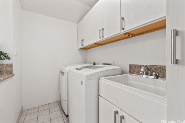 clothes washing area featuring sink, washer and clothes dryer, cabinets, a textured ceiling, and light tile patterned flooring