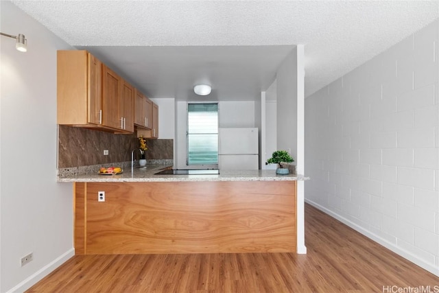 kitchen featuring a textured ceiling, white fridge, light hardwood / wood-style floors, sink, and kitchen peninsula