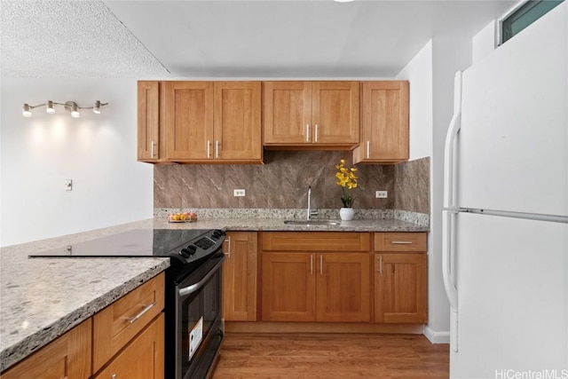 kitchen with white refrigerator, tasteful backsplash, light hardwood / wood-style floors, sink, and electric range