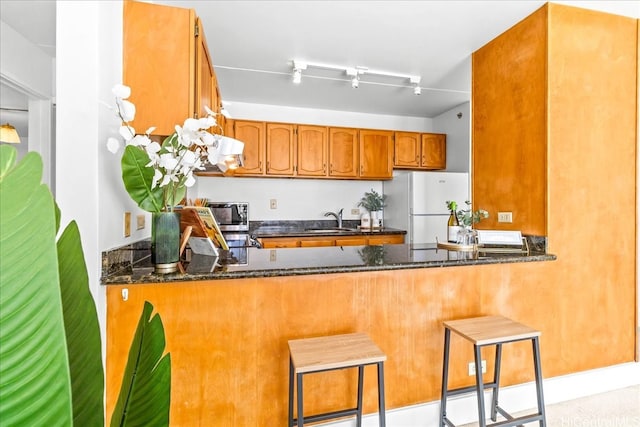 2522 Date St Unit 304, Honolulu, HI 96826 - kitchen with freestanding refrigerator, a sink, a peninsula, brown cabinets, and dark stone counters