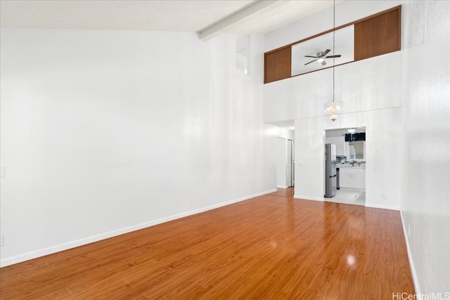 unfurnished living room featuring ceiling fan, high vaulted ceiling, beam ceiling, and light hardwood / wood-style flooring