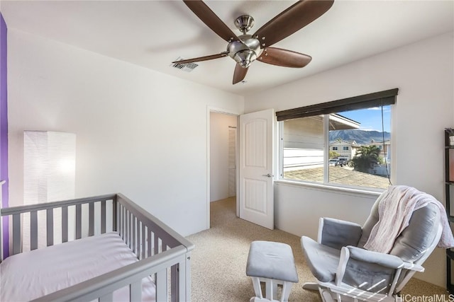 carpeted bedroom with ceiling fan and a nursery area