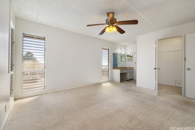 unfurnished bedroom with ceiling fan, a textured ceiling, a walk in closet, and light carpet