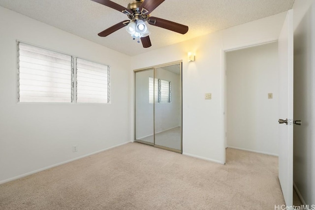 unfurnished bedroom with ceiling fan, light colored carpet, a textured ceiling, and a closet