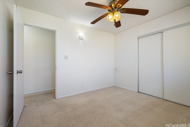 unfurnished bedroom with ceiling fan, light colored carpet, a closet, and a textured ceiling