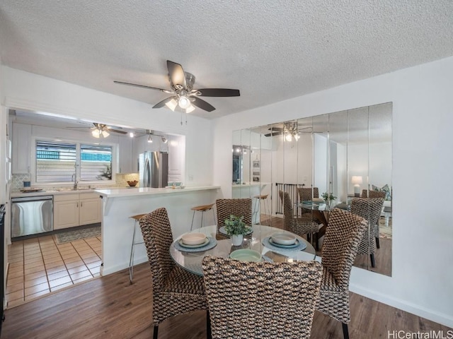 dining area featuring ceiling fan, light hardwood / wood-style floors, sink, and a textured ceiling