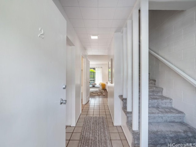 corridor with light tile patterned flooring and a paneled ceiling