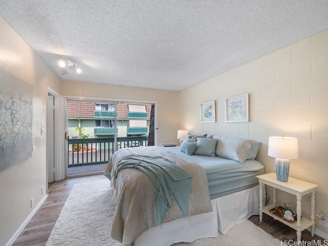 bedroom featuring access to exterior, hardwood / wood-style flooring, and a textured ceiling