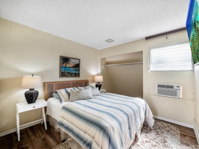 bedroom with an AC wall unit, dark wood-type flooring, a textured ceiling, and a closet