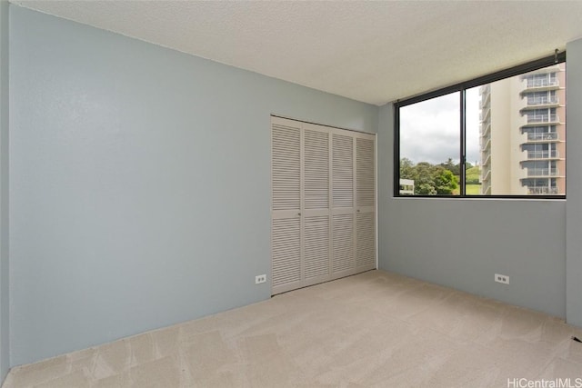 unfurnished bedroom with light colored carpet, a textured ceiling, and a closet