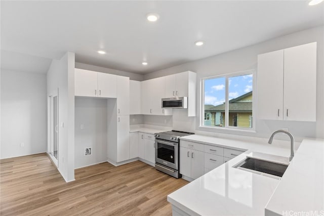 kitchen featuring appliances with stainless steel finishes, light countertops, a sink, and light wood finished floors