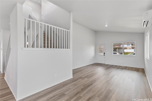 empty room featuring vaulted ceiling, a wall unit AC, and wood finished floors