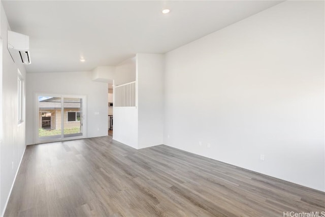 unfurnished room featuring lofted ceiling, light wood-type flooring, and a wall unit AC