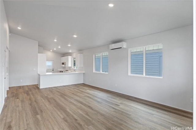 unfurnished living room with a wall mounted AC, vaulted ceiling, and light hardwood / wood-style flooring