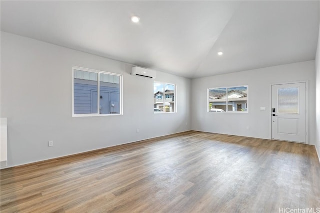 spare room featuring vaulted ceiling, an AC wall unit, and light wood-type flooring