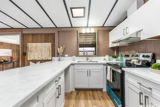 kitchen featuring stainless steel electric range, white cabinetry, sink, light stone counters, and light hardwood / wood-style flooring