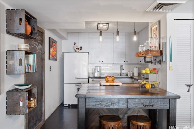 kitchen with hanging light fixtures, backsplash, white cabinetry, wood counters, and white fridge