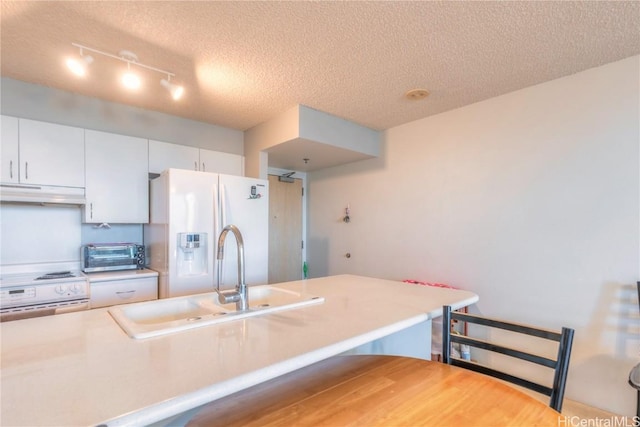 kitchen featuring white appliances, a kitchen bar, a textured ceiling, white cabinetry, and sink