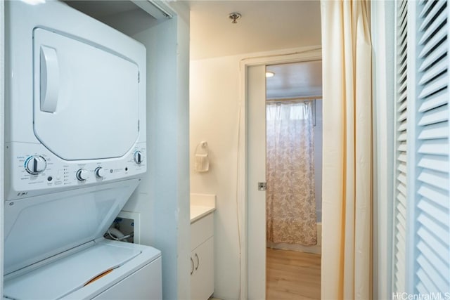 clothes washing area featuring wood-type flooring and stacked washing maching and dryer