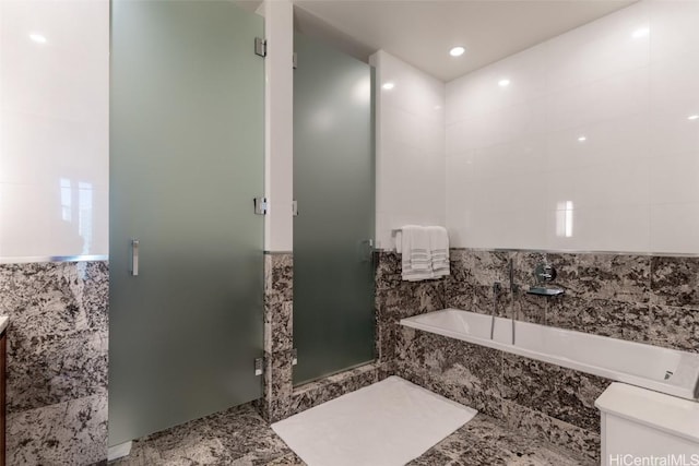 bathroom with tile walls and shower with separate bathtub