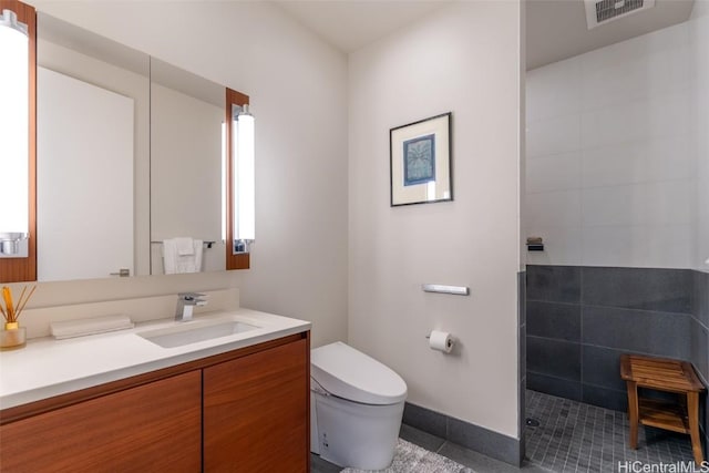 bathroom with toilet, vanity, tiled shower, and tile patterned flooring