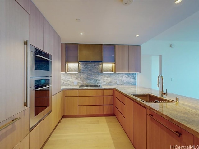 kitchen with kitchen peninsula, light brown cabinets, appliances with stainless steel finishes, sink, and light wood-type flooring