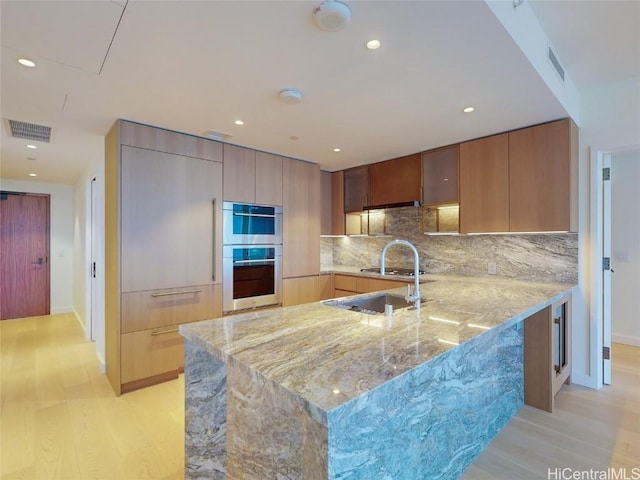 kitchen featuring light stone counters, stainless steel double oven, kitchen peninsula, and light wood-type flooring