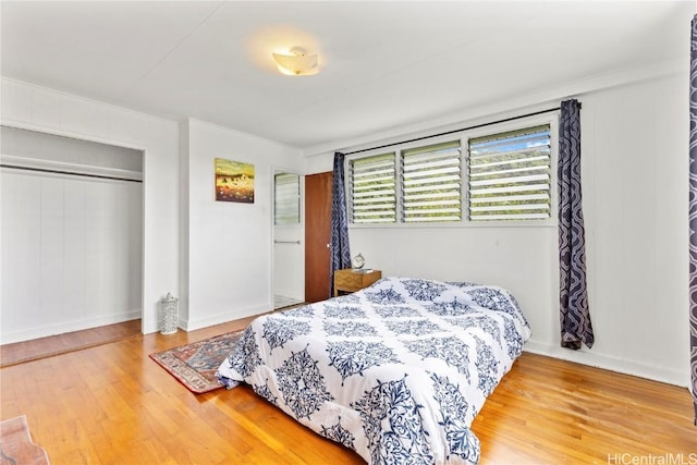 bedroom featuring baseboards, a closet, wood finished floors, and crown molding