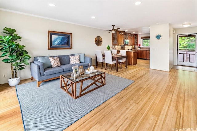 living room featuring ceiling fan, light hardwood / wood-style flooring, ornamental molding, and a healthy amount of sunlight