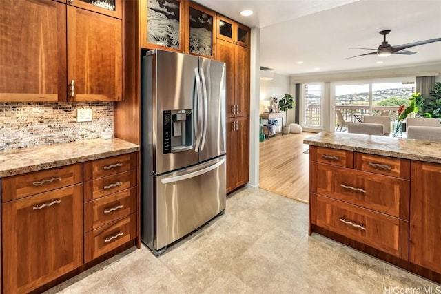 kitchen featuring light stone counters, decorative backsplash, stainless steel fridge, and ceiling fan