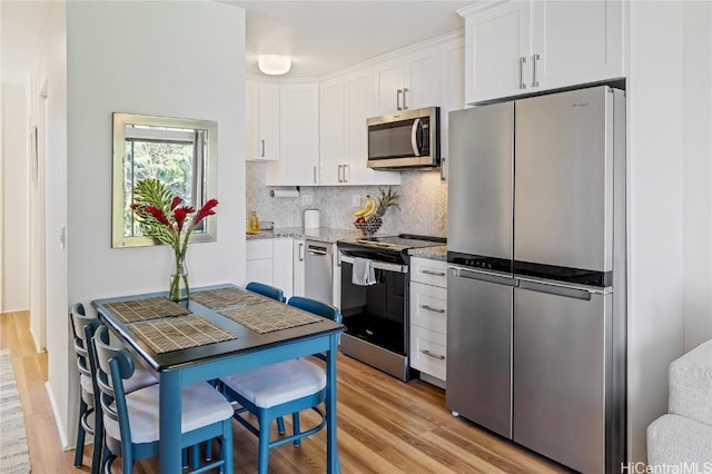 kitchen with stainless steel appliances, white cabinetry, light stone counters, and light hardwood / wood-style floors