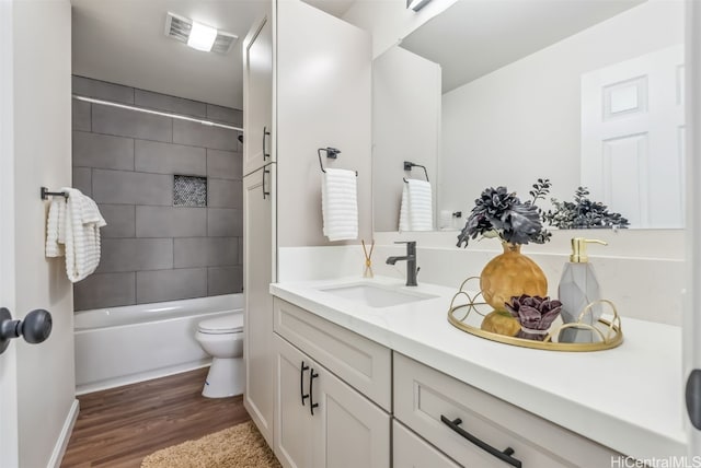 full bathroom with hardwood / wood-style flooring, tiled shower / bath, vanity, and toilet