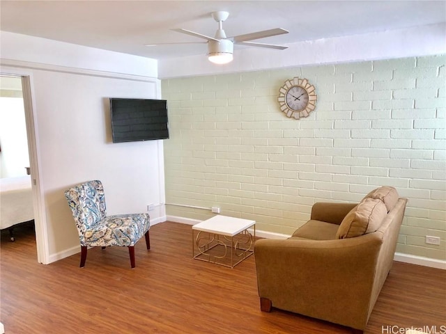 living room featuring wood-type flooring, ceiling fan, and brick wall