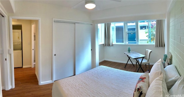 bedroom with dark wood-type flooring, ceiling fan, stacked washer and clothes dryer, and a closet