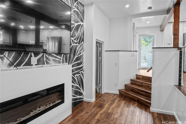 interior space featuring a glass covered fireplace, recessed lighting, wood finished floors, and baseboards