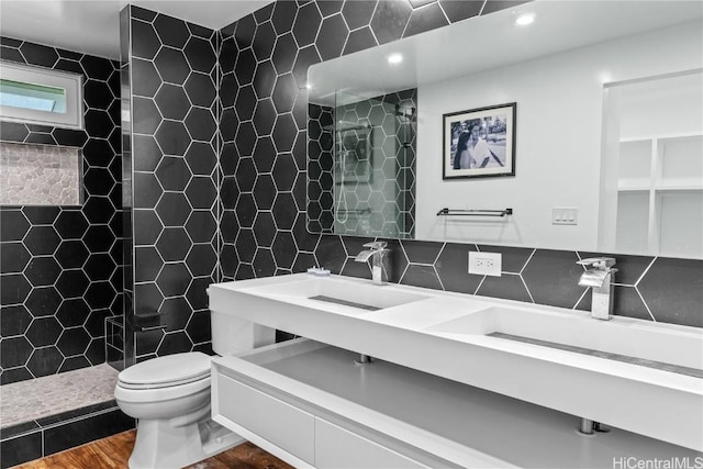 full bath featuring tasteful backsplash, toilet, tiled shower, tile walls, and a sink