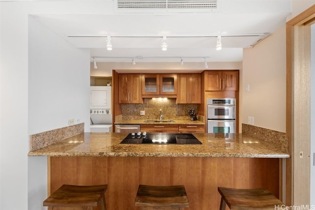 kitchen with stainless steel appliances, stacked washer / dryer, a kitchen breakfast bar, and kitchen peninsula