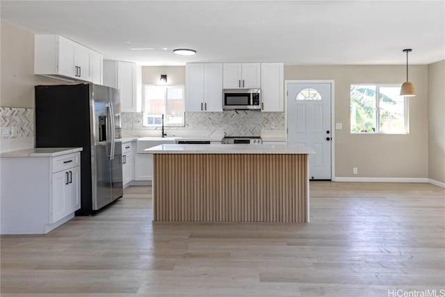 kitchen featuring white cabinets, a kitchen island, pendant lighting, stainless steel appliances, and plenty of natural light