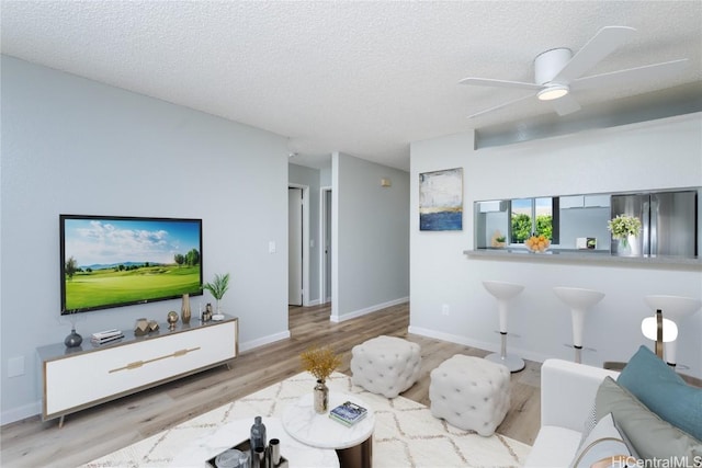 living room with light wood-type flooring, ceiling fan, and a textured ceiling