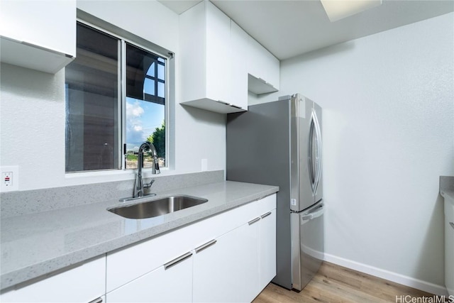 kitchen with light stone countertops, white cabinets, sink, stainless steel refrigerator, and light hardwood / wood-style flooring