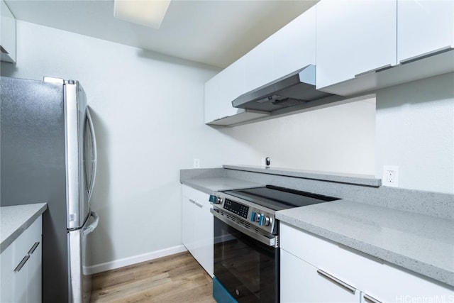 kitchen with wall chimney range hood, stainless steel appliances, white cabinetry, and light hardwood / wood-style flooring