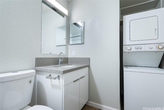 bathroom featuring toilet, stacked washing maching and dryer, and vanity